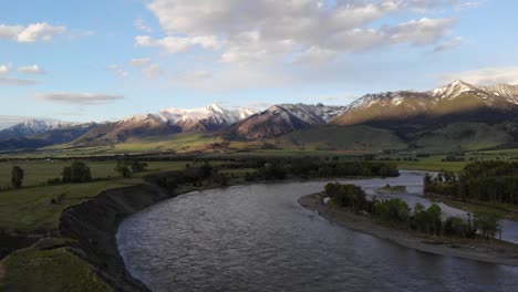 rising drone shot of snowy peaks and green hills near a river bend