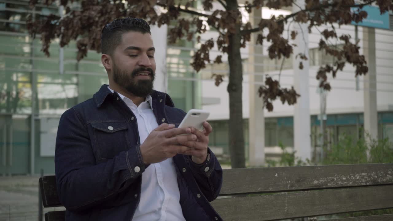 hombre barbudo centrado en la mensajería a través de un teléfono inteligente en la calle