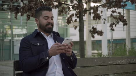 focused bearded man messaging via smartphone on street