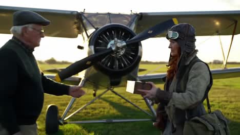 a vintage aviation encounter: a pilot and an elderly man exchange a special package next to a classic airplane in the golden hour light