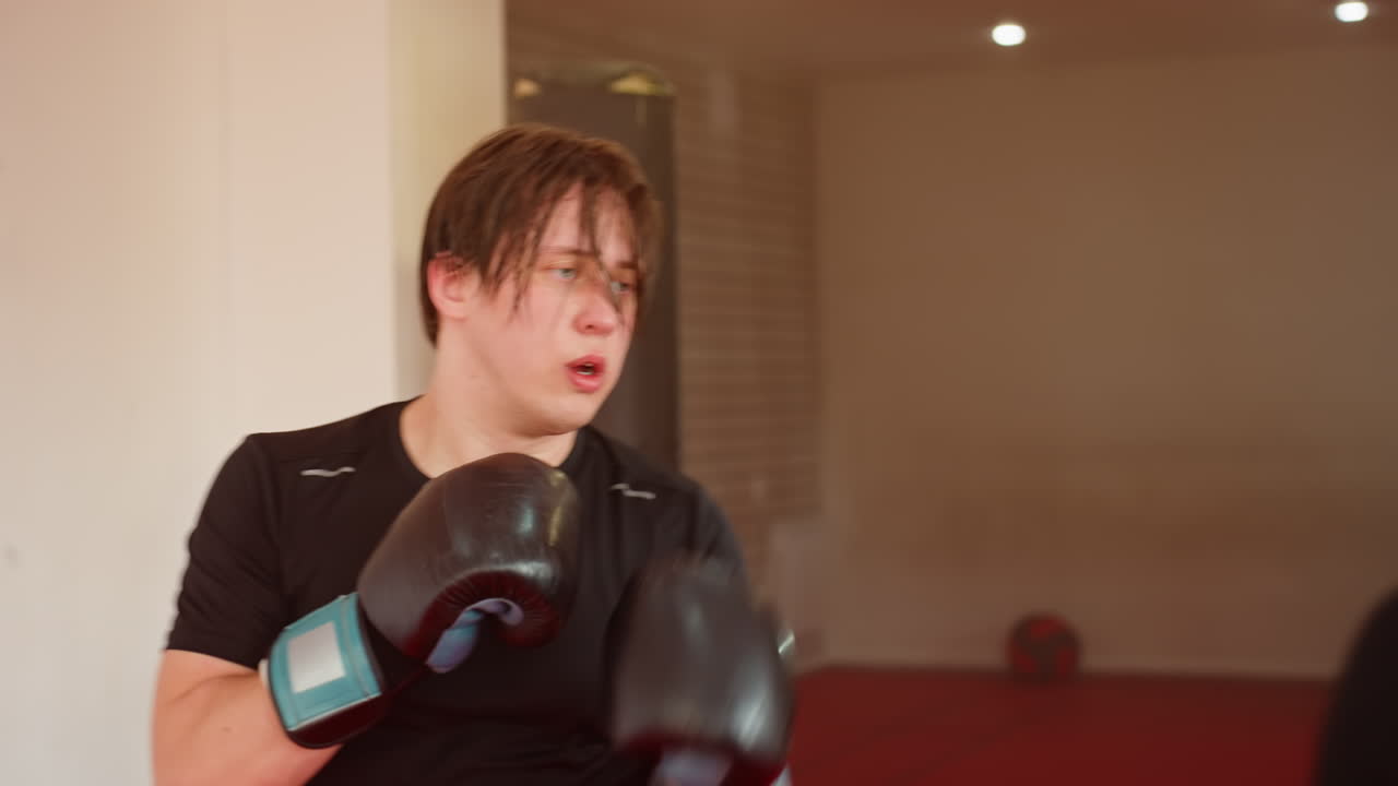 MMA fighter in black sportswear and gloves standing in gym with focused expression preparing for sparring session, sweating under bright lights while practicing stance during training workout