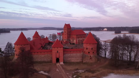 aerial: drone shot of gotic style medieval trakai island castle with purple evening light color casting on the walls from sunset