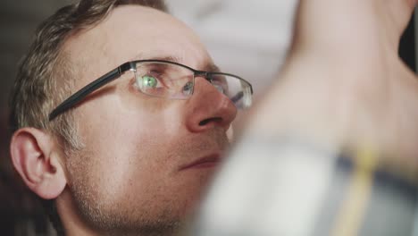 an extreme close-up on the face of a man concentrating on his work. the computer monitor and data are reflected in his glasses. a concept of focus, analysis, and technology
