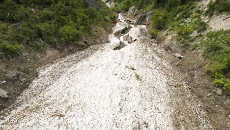 Aerial-view-rising-over-glacial-riverbed-overlooking-craggy-Utah-ice-caves-opening