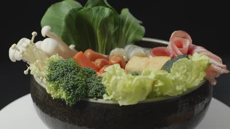 close up of a pot of shabu ingredients spinning around on white table in the black background kitchen