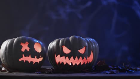 Video-of-halloween-carved-pumpkins-and-smoke-with-copy-space-on-blue-background