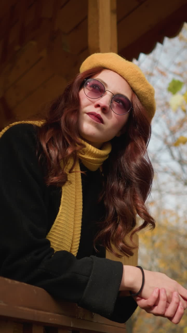 dama feliz tocando su cabello lúdicamente mientras descansa su mano en la cuña del mirador, rodeada por un telón de fondo vibrante de árboles de otoño