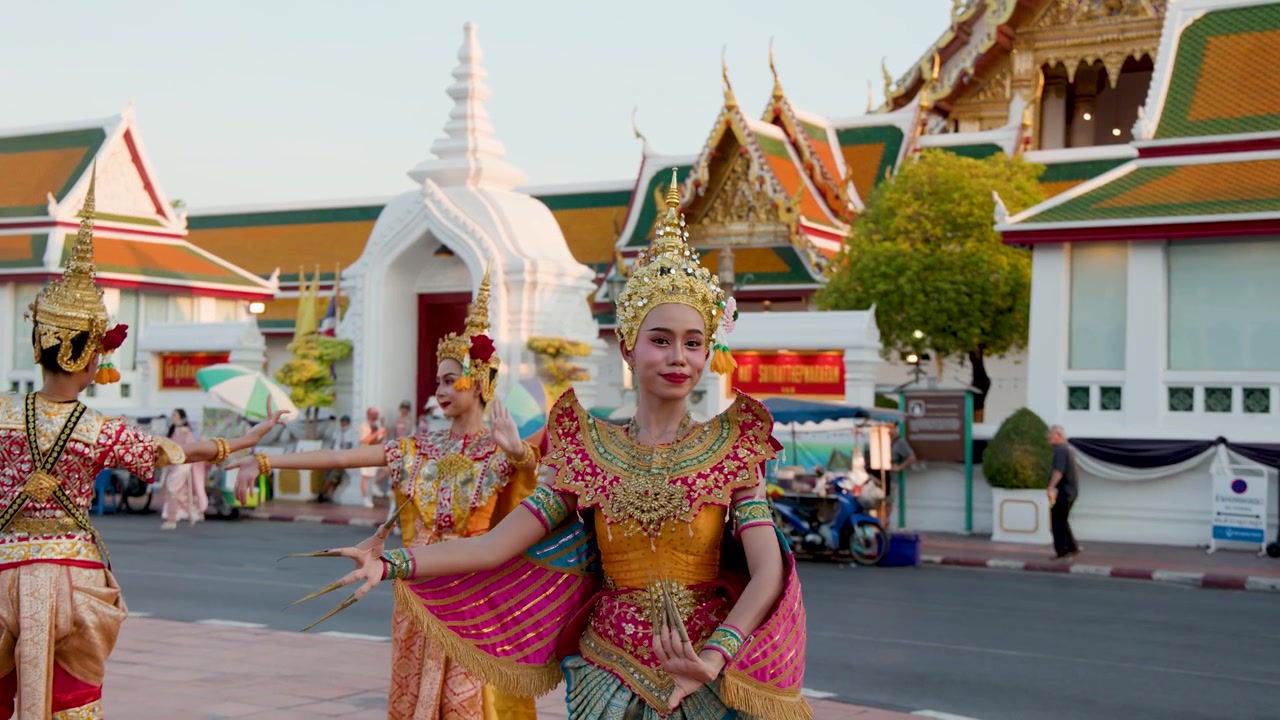Artisti thailandesi in sontuosi costumi dorati e copricapi chada danzano all'esterno di un tempio storico