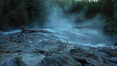 Aerial-drone-shot-flying-in-slow-motion-over-the-dark-wet-rocks-and-misty-waterfall-at-Big-Wilson-Falls-during-dusk-in-Maine