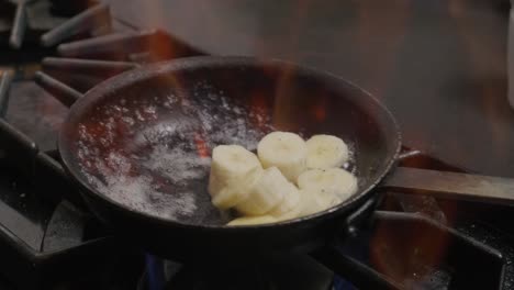 pouring liquid into a pan of bananas cooking with fire