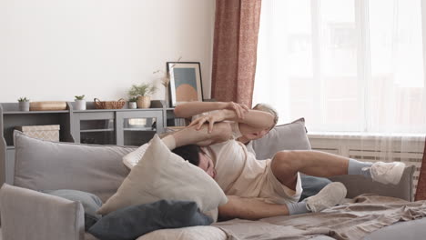 two young men fighting with pillows on sofa