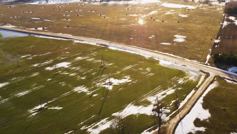 Golden-sunlight-over-early-spring-meadows,-partly-covered-in-snow,-aerial-view