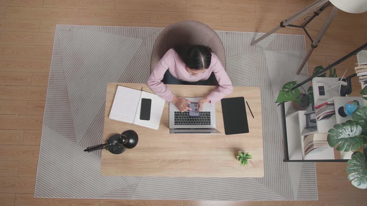 집에서 나무 책상에 앉아있는 동안 스마트폰을 사용하는 여성의 상단 시각