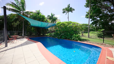 pullback across large outdoor pool area shimmering reflecting sunlight with shade cloth in fenced area