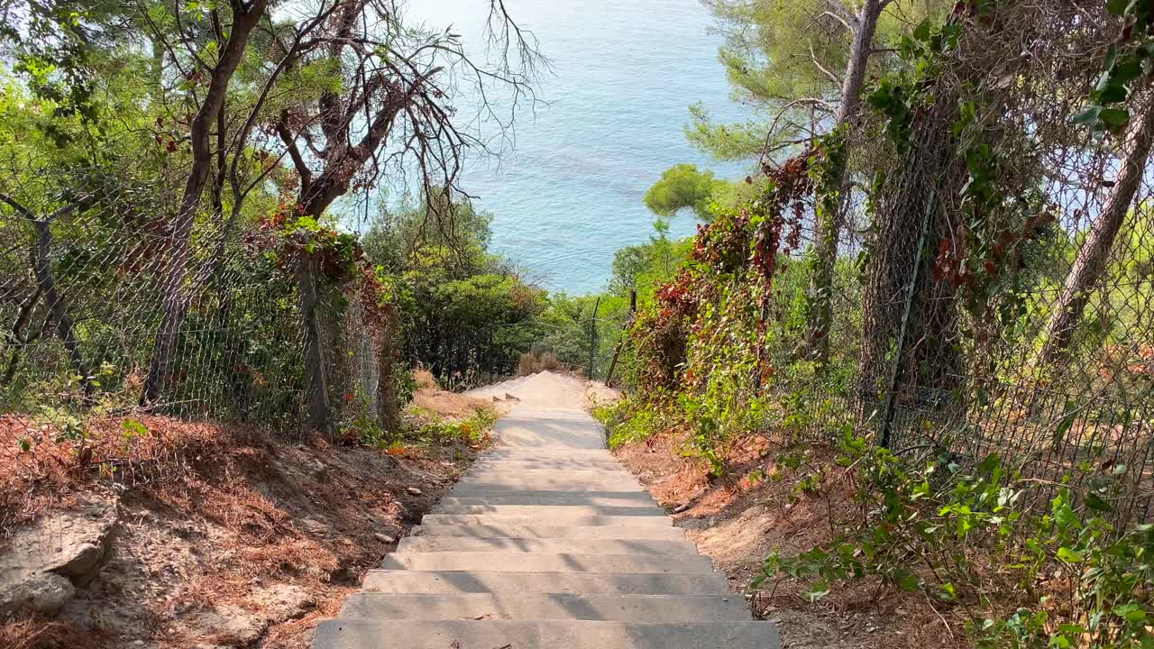 Beautiful stairs going down to the beach with big trees and sea view in Cavali&egrave;re Lavandou South of France, magical green nature hike near water, holiday vacation, 4K shot