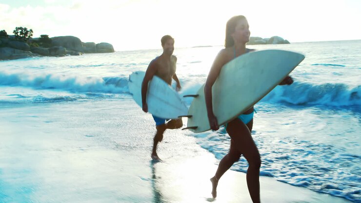 Couple running on beach with surfboard