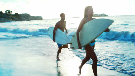 pareja corriendo en la playa con una tabla de surf