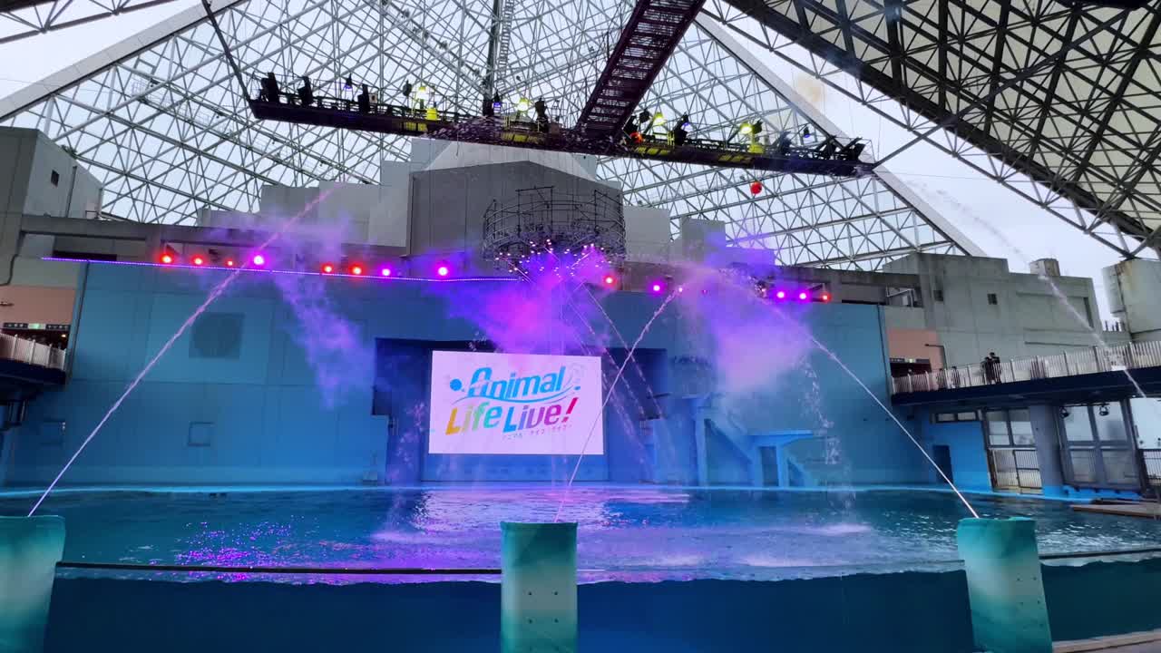 Colorful stage show at Tokyo aquarium with water sprays and lights under a glass roof