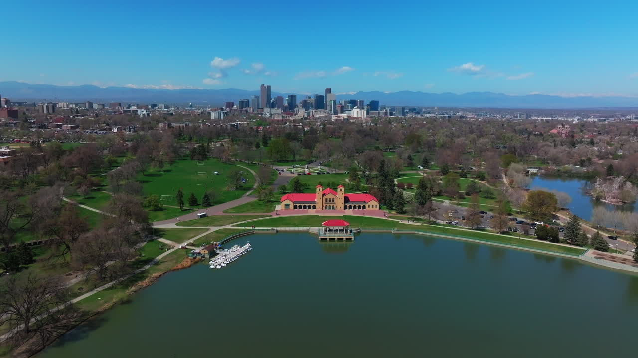 City Park Denver Colorado Lake Pavilion vibrant blossom spring summer aerial drone sunny blue sky snow capped Rocky Mountains front range cityscape green lush grass trees forward upwards motion