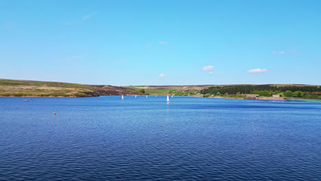 Winscar-Reservoir-in-Yorkshire-becomes-a-magical-setting-for-a-thrilling-boat-race,-as-small-one-man-boats-adorned-with-white-sails-skim-across-the-tranquil-blue-lake