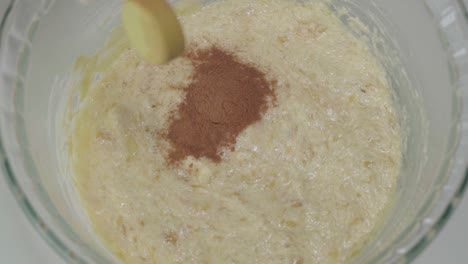 adding teaspoon of cinnamon to yellow batter, closeup directly above