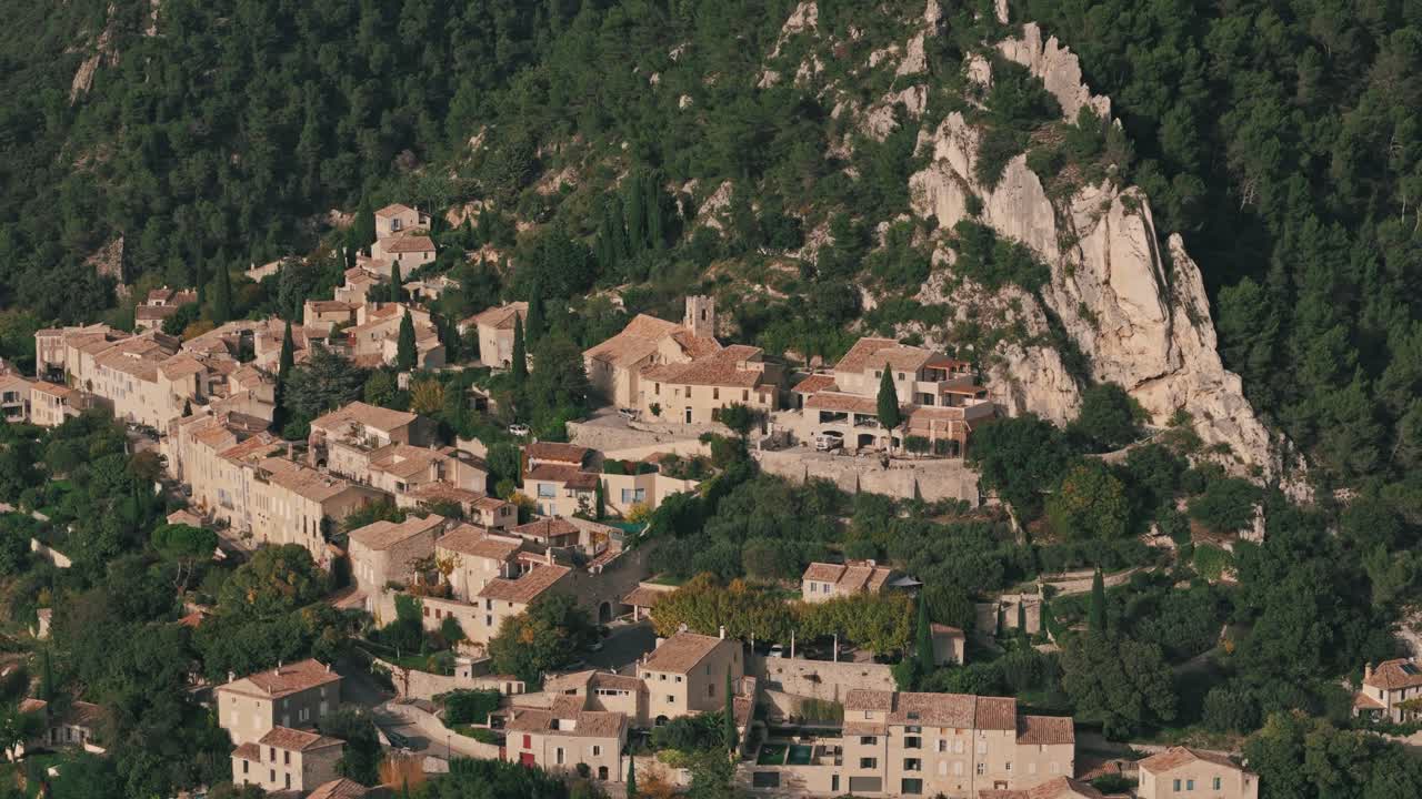 フランス、プロヴァンス地方セギュレの、森に囲まれた山腹に建つ趣のある中世の家々の上空を左旋回する空撮。村の魅力的な建築と美しい丘が広がる。