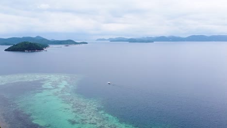 Rising-aerial-view-of-ocean,-coral-reef-ecosystem,-fishing-boat-and-tropical-islands-in-Coron-Bay,-Palawan,-Philippines,-Southeast-Asia