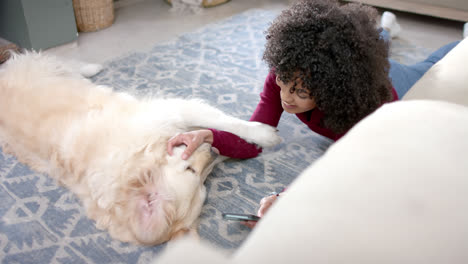 happy biracial woman with golden retriever dog using smartphone at home, slow motion