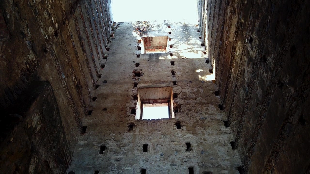 Vista para cima entre altas paredes de pedra em ruínas na Hacienda Coahuixtla em Morelos, México, revelando alvenaria desgastada, detalhes arquitetônicos antigos e céu claro acima da estrutura abandonada