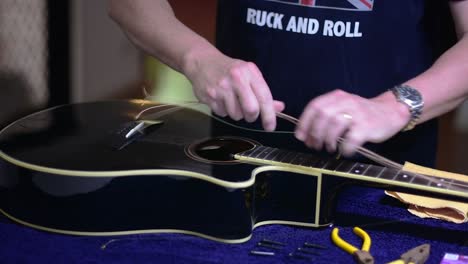 encordando y limpiando una hermosa guitarra acústica negra de un solo corte - quitando las cuerdas del extremo del puente