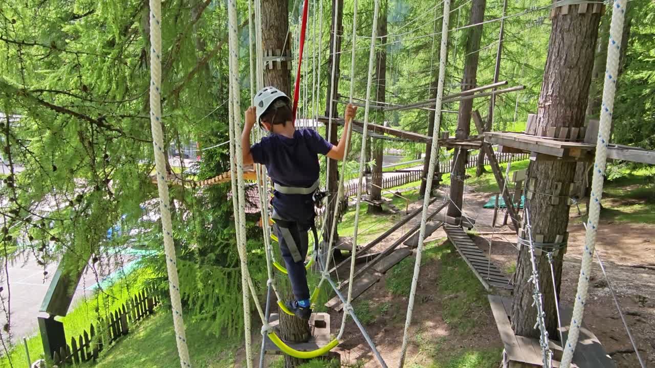 Slow motion rearview of child navigating a forested via ferrata in Alta Badia, Dolomites, Italy