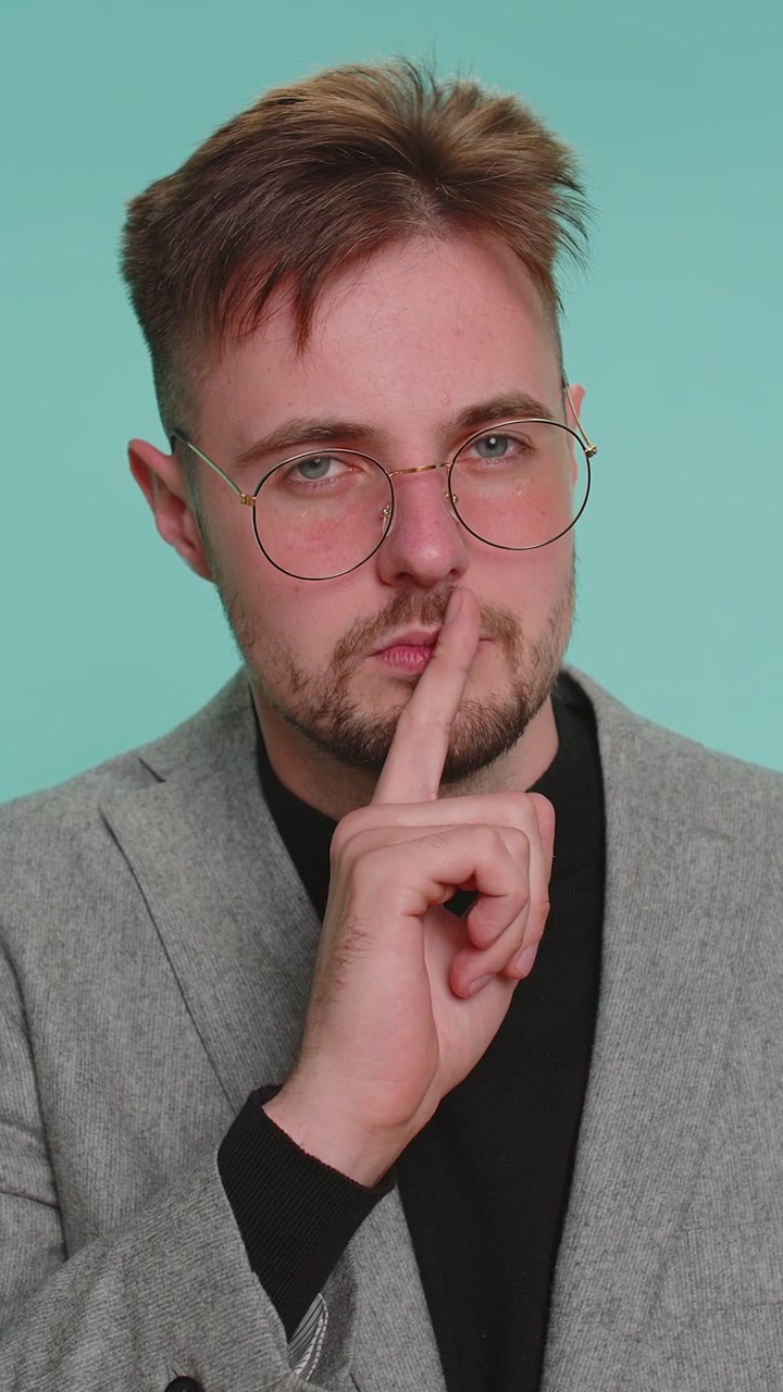 Young man presses index finger to lips makes silence gesture sign do not tells secret shh be quiet