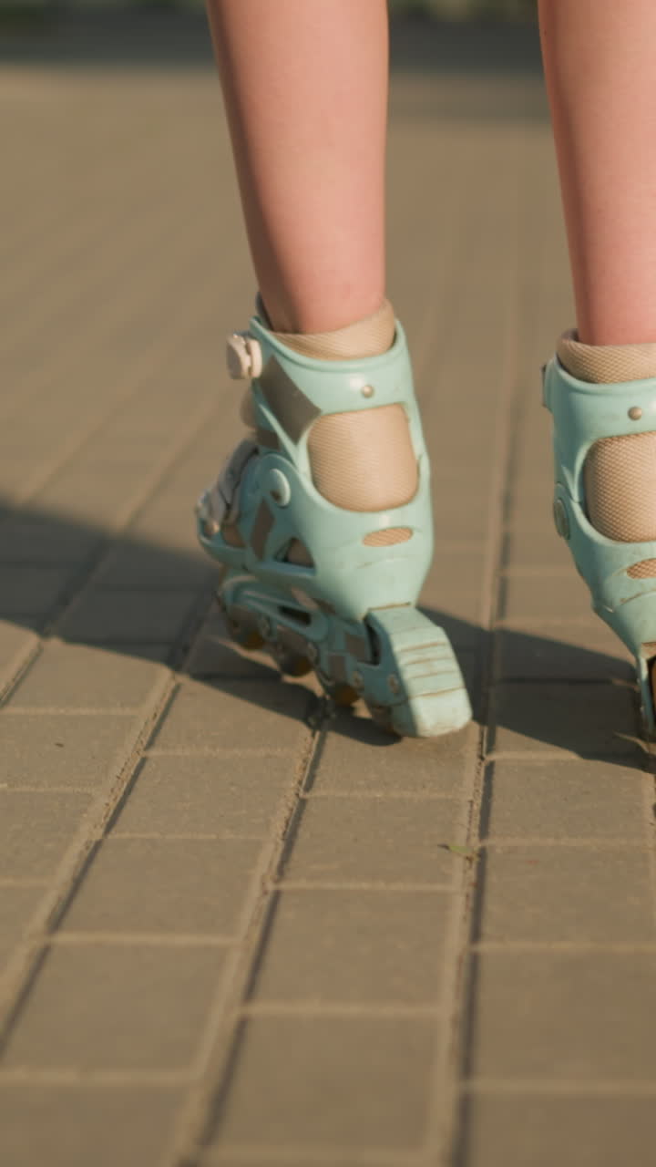 Back leg view of person skating along interlocked path on rollerblades, shadows extending on ground, with soft focus on blurred background and warm sunlight