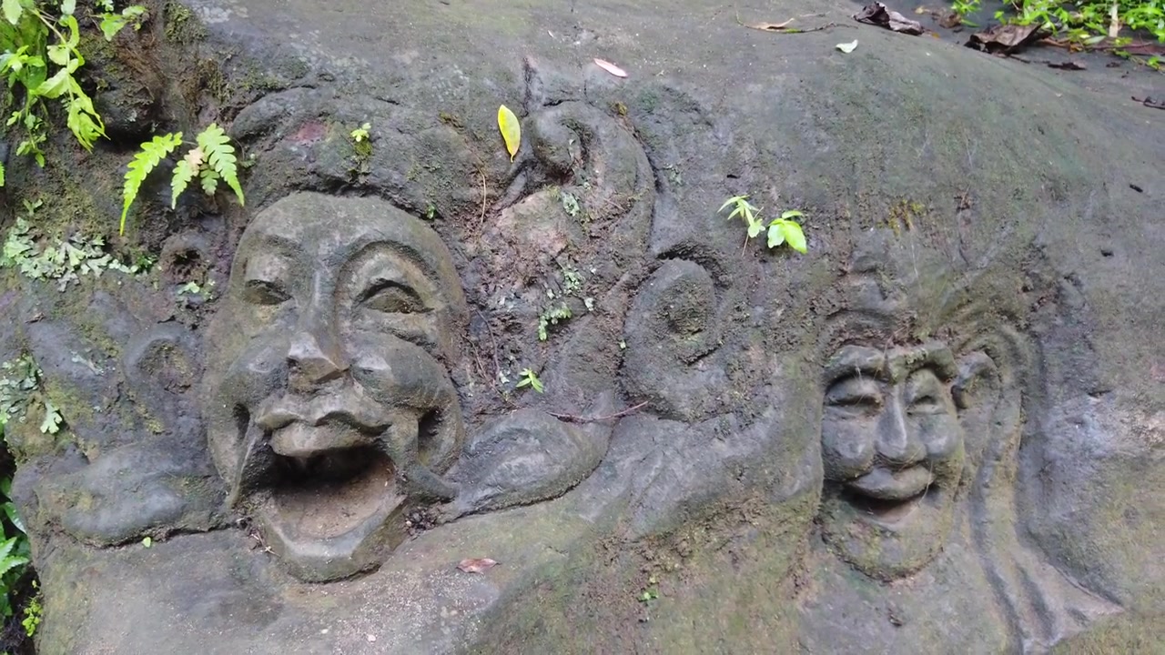 Primo piano di antiche sculture rupestri di volti sul fiume Petanu, Goa Gajah, Ubud, Bali, Indonesia