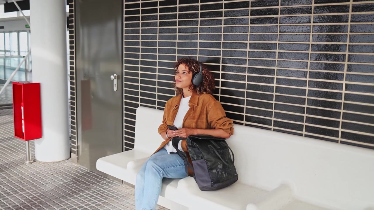 Giovane donna con le cuffie che cammina e si siede in una moderna stazione della metropolitana