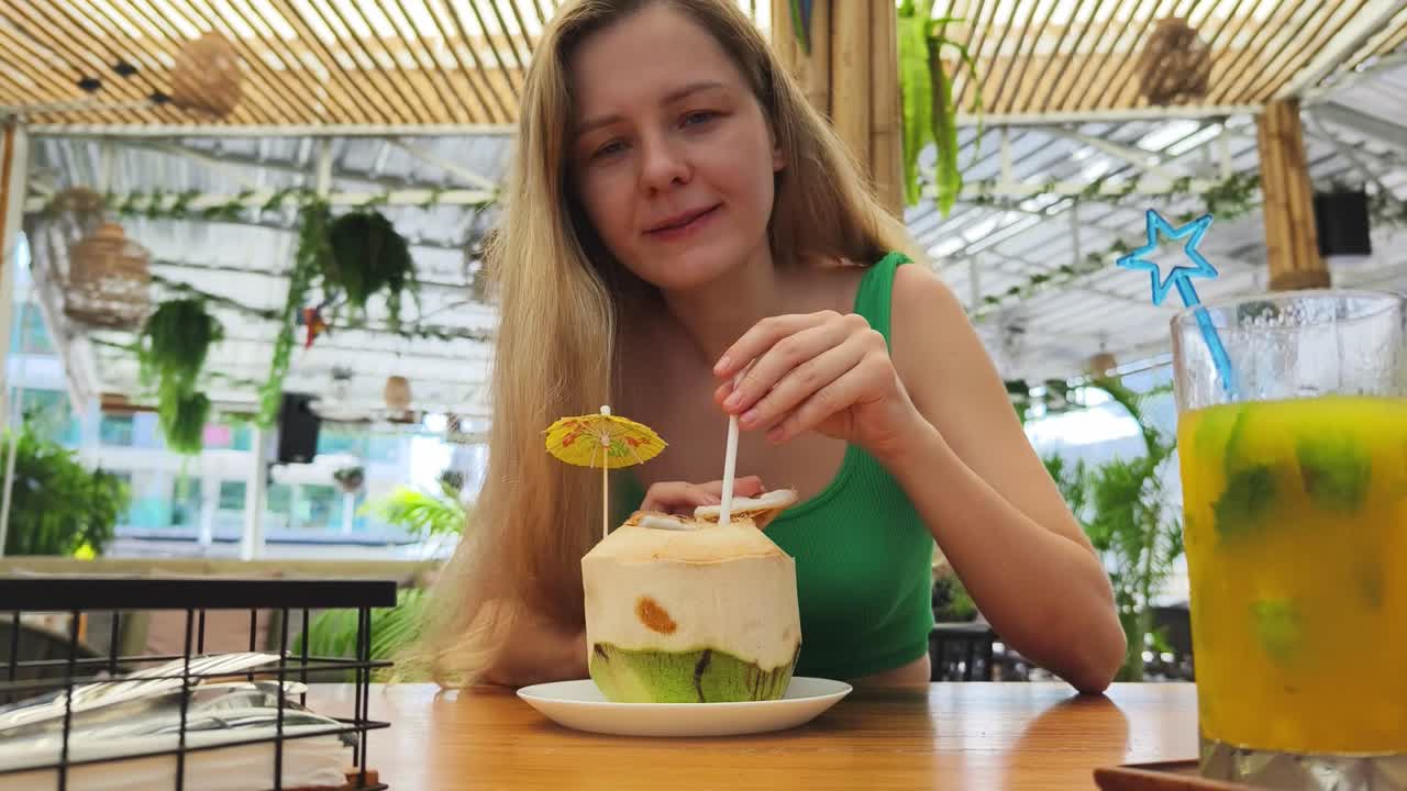 mujer disfrutando de una bebida de agua de coco en un café tropical
