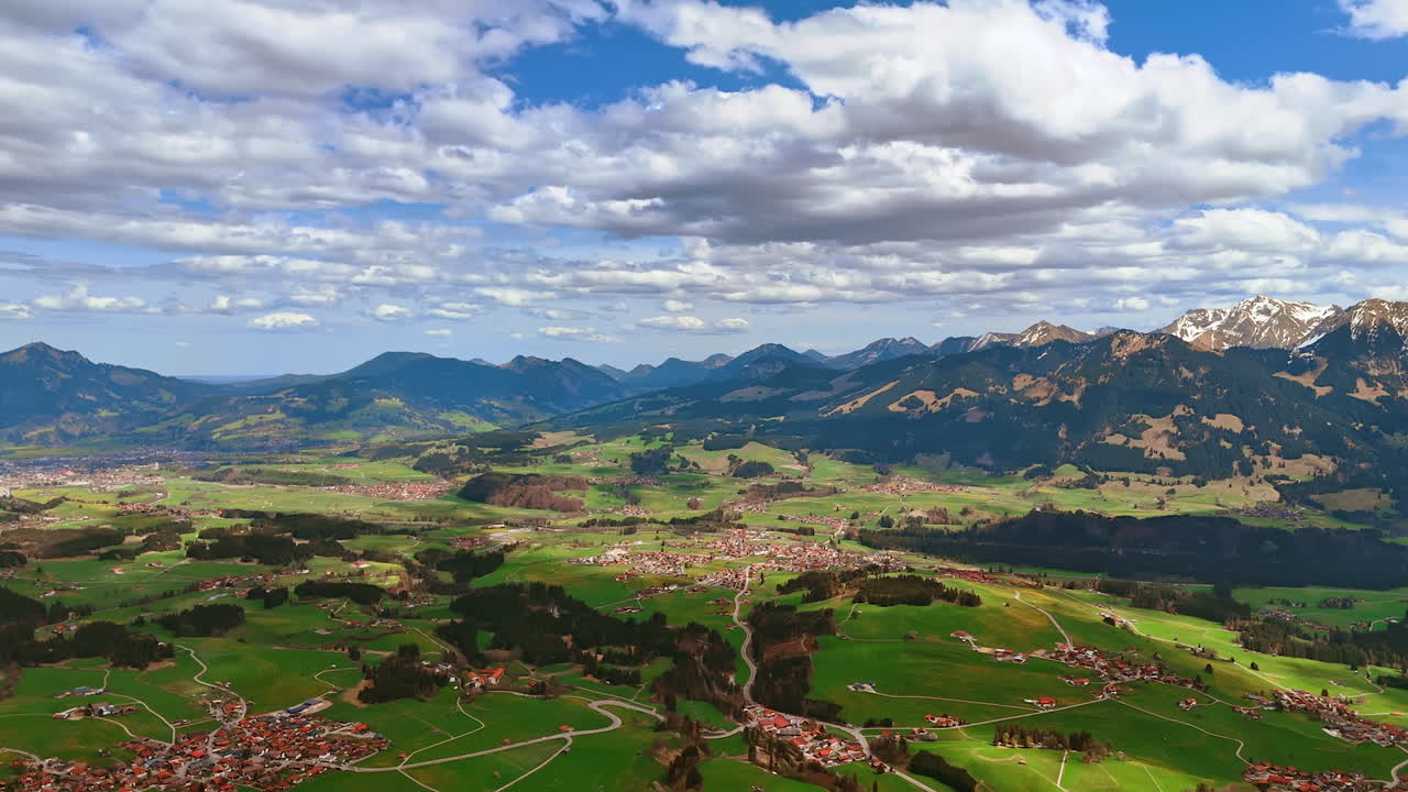 Beautiful mountains surround the picturesque valley with inhabited areas and forests. Aerial perspective on Bolsterlang, Bavaria, Germany under the cloudy sky.