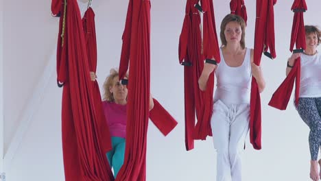 relaxed women group sits and rests in red fly yoga hammocks