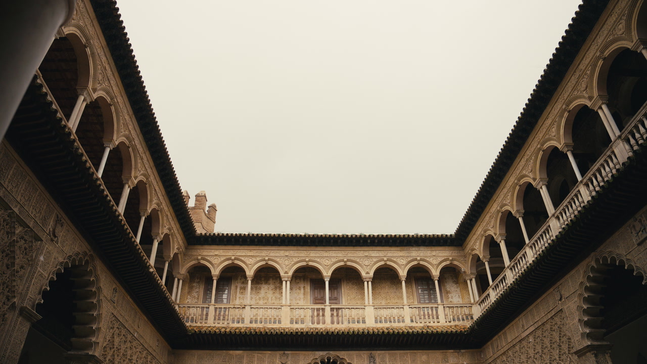 Symmetrical courtyard view inside Real Alcazar in Seville, Spain, featuring detailed Moorish arches, historic facades, and open sky creating a balanced architectural composition.