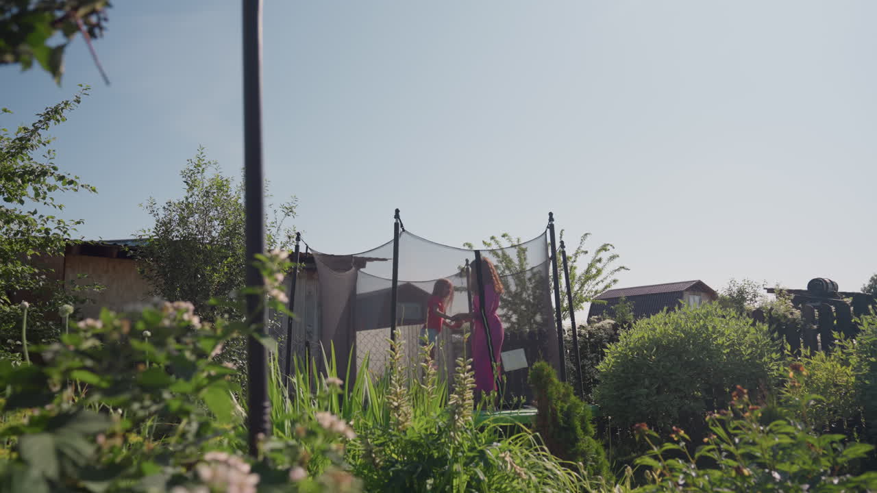 Mother And Daughter Having Fun Outside, Joyful Outdoor Exercise As Mother Watches Daughter Bounce Happily, Vibrant Backyard Energy With Mother Overseeing Playful Bouncing On Trampoline