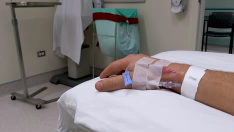 movimientos lentos de la mano de la mano derecha masculina caucásica irreconocible en un escenario médico con iv en la muñeca