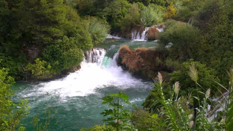 large waterfall pouring from one blue pond to another blue pond in krka national park in croatia