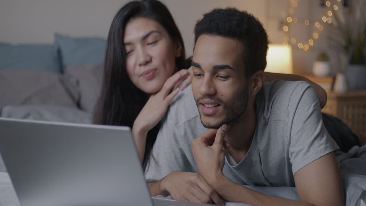 una pareja viendo una computadora portátil en la cama.