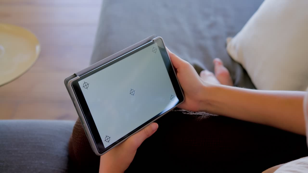Afroameričanka držící tablet na gauči, klepající na rohové značky a naklánějící jej, aby se vyhnula odleskům.