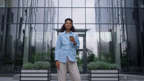 Satisfied-finance-manager-smiling-holding-hot-coffee-cup-in-empty-business-yard.