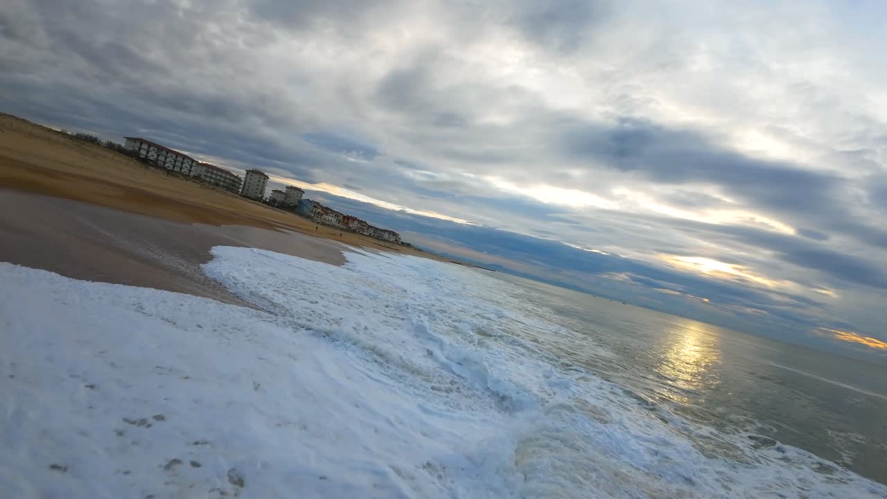vuelo en primera persona sobre las olas en la salvaje playa de surf de hossegor durante una puesta de sol nublada