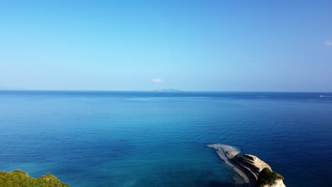 Vista-Aérea-De-La-Isla-De-Corfú-En-Un-Soleado-Y-Cálido-Día-De-Verano-Con-Un-Cielo-Azul-Claro-Y-Aguas-Cristalinas-Del-Océano