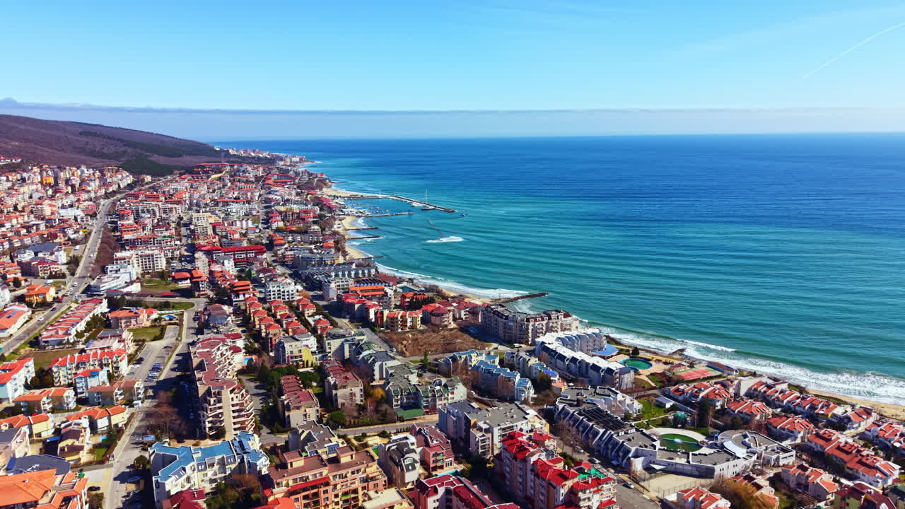 Vista di una città costiera con edifici lungo la spiaggia sotto un cielo sereno di giorno, che mostra l'acqua e la costa.