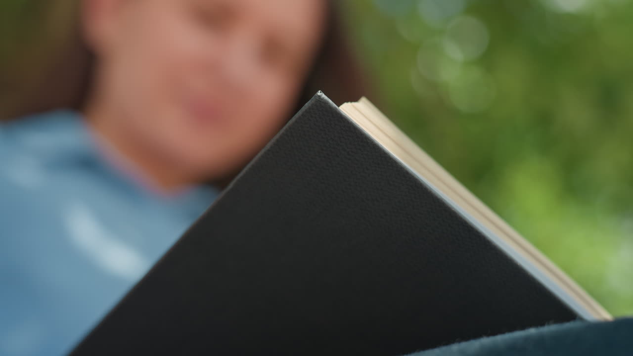 Mujer caucásica hojea un diario con tranquilidad, señora examina un diario con atención bajo ramas frondosas, mujer de aspecto caucásico explora con calma un diario sentada bajo árboles extensos