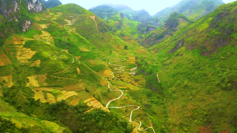 Aerial-tilt-down-of-a-winding-road-cut-into-the-mountainside-of-the-misty-mountains-of-Ma-Pi-Leng-Pass-in-northern-Vietnam